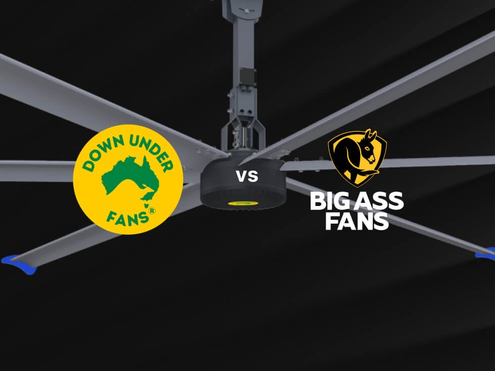 Close-up of a large ceiling fan with two logos: "Down Under Fans" on the left and "Big Ass Fans" on the right, against a dark background.