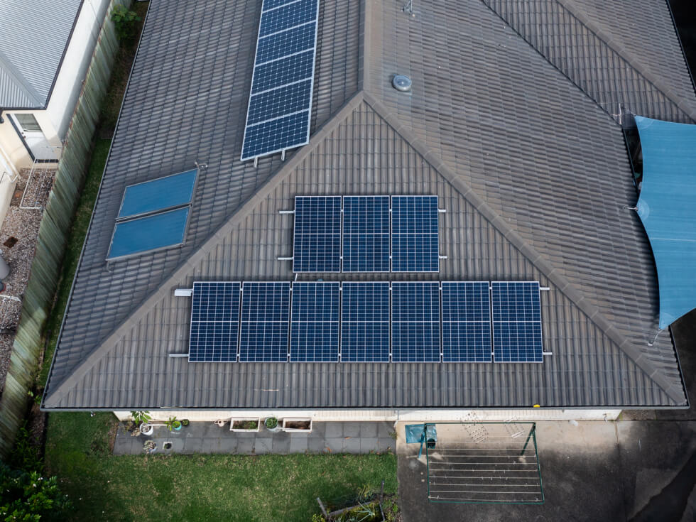 Aerial view of a house roof with multiple solar panels installed, next to a skylight.