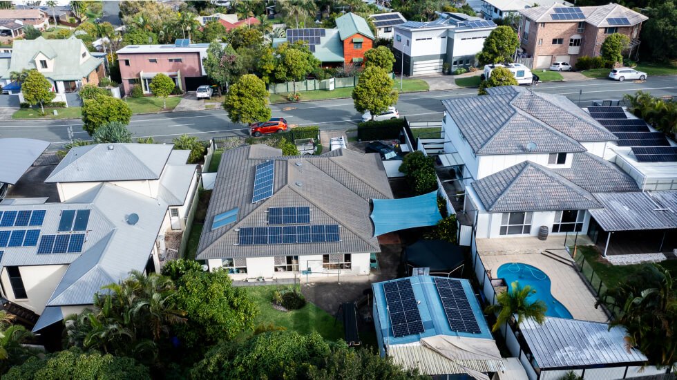 A suburban neighborhood located on the Sunshine Coast in Australia with houses featuring solar panels on their roofs, a blue car on the street, and a backyard pool visible in one property.