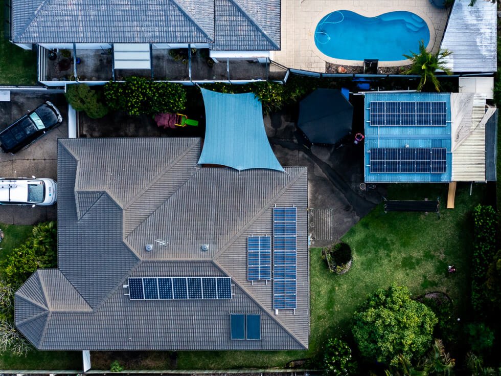 Aerial view of a Sunshine Coast residential property featuring solar panels on the house and an adjacent building, a backyard with a canopy, and a blue swimming pool.